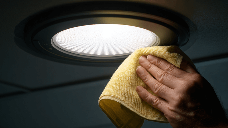 A person carefully cleaning a dusty LED downlight with a soft cloth