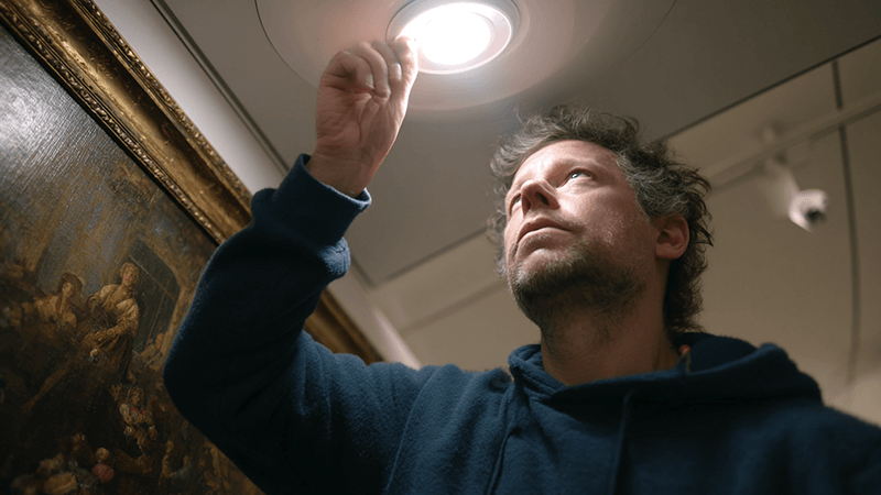 A lighting designer adjusting an adjustable LED downlight in a gallery to highlight a specific painting.