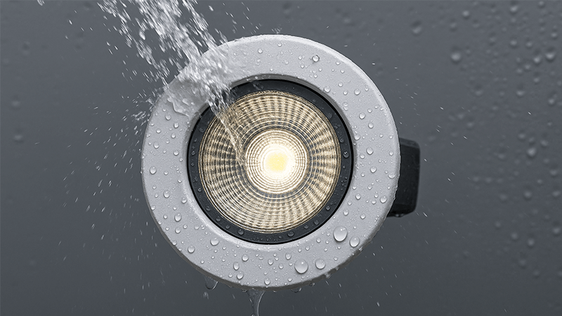 A close-up of an IP65 rated downlight being sprayed with water to demonstrate its water resistance